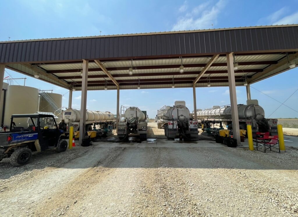 Multiple tanker trucks parked under a covered structure with industrial equipment.